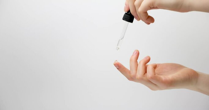 Hand of woman with pipette drop of serum or hyaluronic acid on gray background. Hands of a beautiful woman dripping serum collagen.