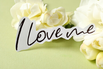 Piece of paper with handwritten phrase I Love Me  and flowers on light background, closeup