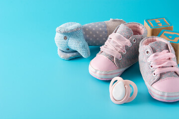 Baby rompers, shoes, feeding bottle, pacifier and toy on blue background. Copy space