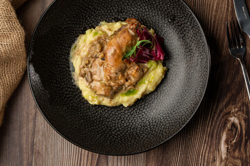 Baked meat and mashed potatoes served with mushrooms, green sauce and lettuce in black bowl. Close-up on a wooden background with a sacking and silver cutlery by side. Top view.