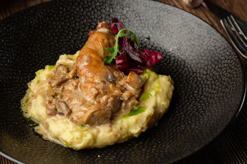 Baked meat and mashed potatoes as a garnish served with mushrooms, green sauce and lettuce in black bowl. Macro close-up on a wooden background. Delicious meal, restaurant menu concept.