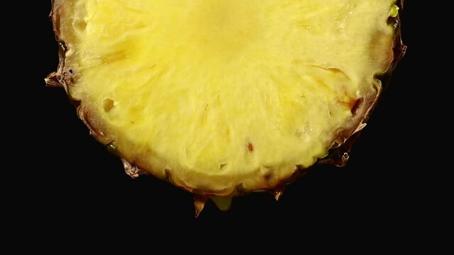 freshly squeezed pineapple juice drops from the ripe yellow fruit slice close - up on a black background slow motion zoom in