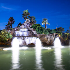 Naklejka premium Colourful water fountain at night dark blue skies green palms 