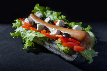 Greek hot dog with homemade sausage with cheese, tomatoes, lettuce on a black background