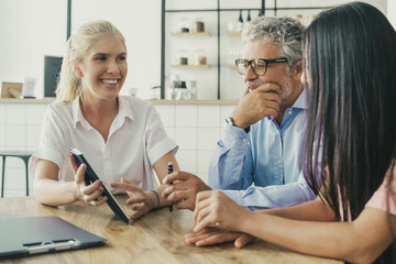 Cheerful female manager and young and mature customers watching and discussing presentation on...