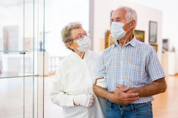 Obraz premium mature couple in mask protecting against covid examines paintings on display in hall of art museum