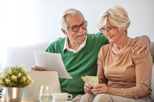 Front View Smiling Old Woman Entering Payment Data Into Banking Application On Computer While Pleasant Mature Husband Reading Paper Tax Document. Happy Senior Married Couple Managing Family Budget.