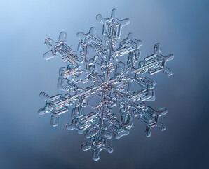 Snowflake on smooth gradient background. Macro photo of real snow crystal on glass surface. This is small snowflake with unusual pattern.