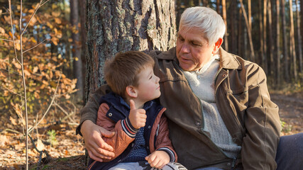 Happy child with Grandfather playing at the forest. Grandpa retiree. Retirement parent. Portrait of pensive senior man  and his grandson. Senior man having fun with his grandchild outdoor.