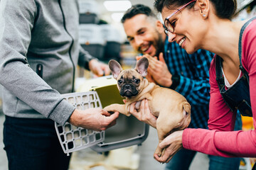 Happy couple buying transport box for their French bulldog puppy in pet shop.