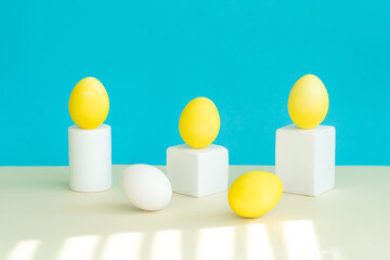 Obraz premium In the foreground lies a yellow egg in the background is geometric figures, on a pedestal, there are yellow eggs. Selective focus.