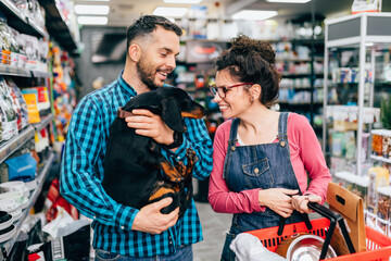 Fototapeta na wymiar Happy couple buying toys and food for their Dachshund in pet shop.