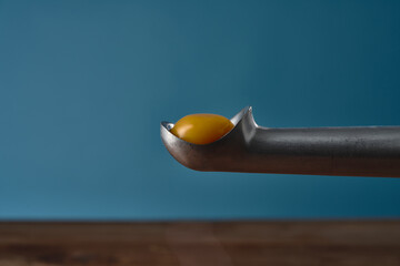 Egg yolk on an ice cream spoon on wooden table with blue background