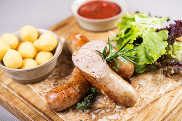 portion of tasty grilled homemade sausages with boiled potato, lettuce and savory tomato sauce on wooden board