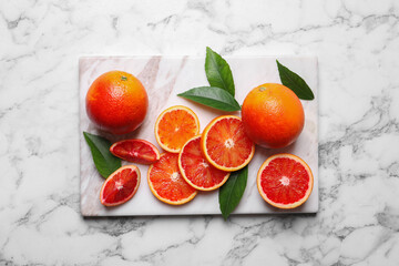 Whole and cut red oranges with green leaves on white marble table, top view