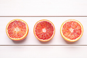 Halves of ripe red oranges on white wooden table, flat lay