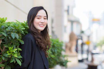A portrait of a long-haired Asian woman wearing a dark blue robe Smiling and happily standing outdoors in the city.