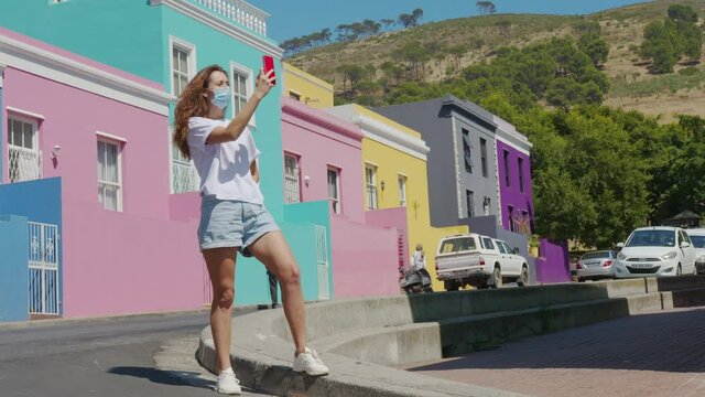 Woman tourist in pandemic shoots on the phone in Cape town Bo-Kaap Malay area, perspective of cobble stone street, colored terrace houses, South Africa.