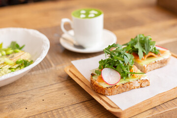 Healthy breakfast in the restaurant. Green salad, bruschetta with arugula and salmon and matcha latte