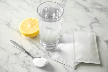 Medicine sachets, glass of water, spoon and lemon on white table