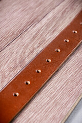 A orange leather belt lies on a brown wood diagonally close-up