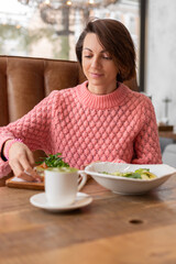 Woman in a restaurant in a cozy warm sweater eating healthy breakfast toast with arugula and salmon