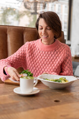 Woman in a restaurant in a cozy warm sweater eating healthy breakfast toast with arugula and salmon