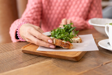 Woman in a restaurant in a cozy warm sweater wholesome breakfast with toast with arugula and salmon