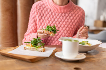 Obraz na płótnie Canvas Woman in a restaurant in a cozy warm sweater wholesome breakfast with toast with arugula and salmon