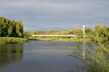 Obraz premium cable-stayed bridge over the river on a sunny summer day with green trees on the river bank.