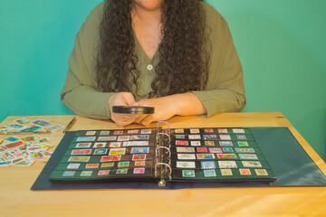 Brunette woman with a magnifying glass looking through her philatelic collection.
