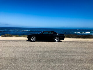 a black car in front of the blue ocean - obrazy, fototapety, plakaty