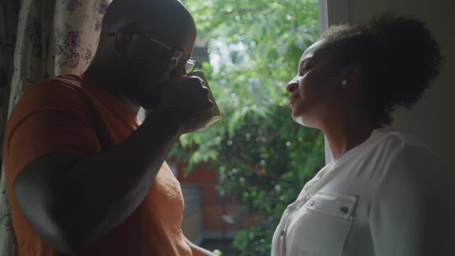 Young Black Couple Having A Cup Of Tea Or Coffee Exchanging Affection And Talking In Front Of The House Window.