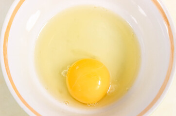 One raw chicken egg is broken into a cup.