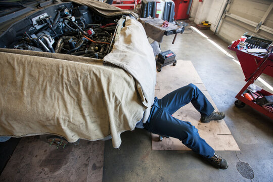 Mechanic lays on a trolley under a car in an auto repair shop