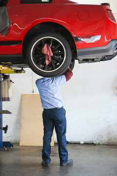 Mechanic in a repair shop works on the underside of a car up on a lift