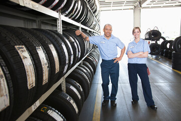 Portrait of smiling male and female mechanic by a rack of tyres in a workshop