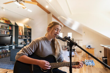 Fourteen year old teenage girl playing her guitar and singing at home in loft space
