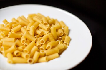 Uncooked rigatoni pasta in the white porcelain plate. Blurry background.