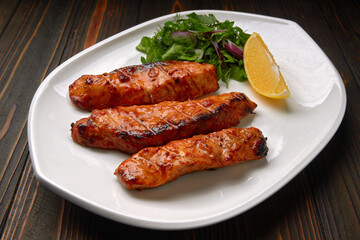 Three grilled pieces of salmon fillet, trout, with herbs and lemon, on a white plate, on a wooden background