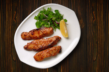 Three grilled pieces of salmon fillet, trout, with herbs and lemon, on a white plate, on a wooden background
