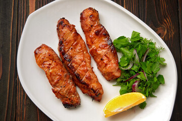 Three grilled pieces of salmon fillet, trout, with herbs and lemon, on a white plate, on a wooden background