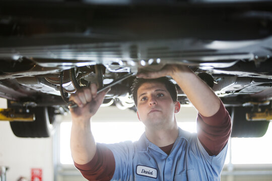 Mechanic in a repair shop works on the underside of a car up on a lift