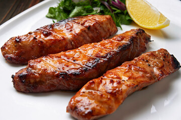 Three grilled pieces of salmon fillet, trout, with herbs and lemon, on a white plate, on a wooden background