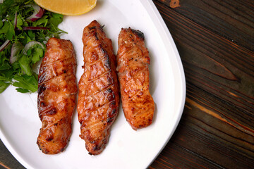 Three grilled pieces of salmon fillet, trout, with herbs and lemon, on a white plate, on a wooden background