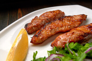Three grilled pieces of salmon fillet, trout, with herbs and lemon, on a white plate, on a wooden background
