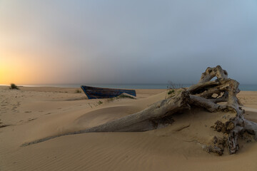 oude houten vissersboot en drijfhout op een strand na zonsondergang met dorpslichten erachter