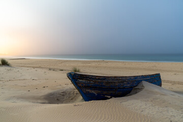 colorful old wooden rowboat buried in the sand on a beach after sunset with colorful sky