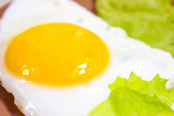 Fried eggs close-up with green lettuce leaves.