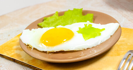 Fried eggs on a plate on the table with a green lettuce leaf.